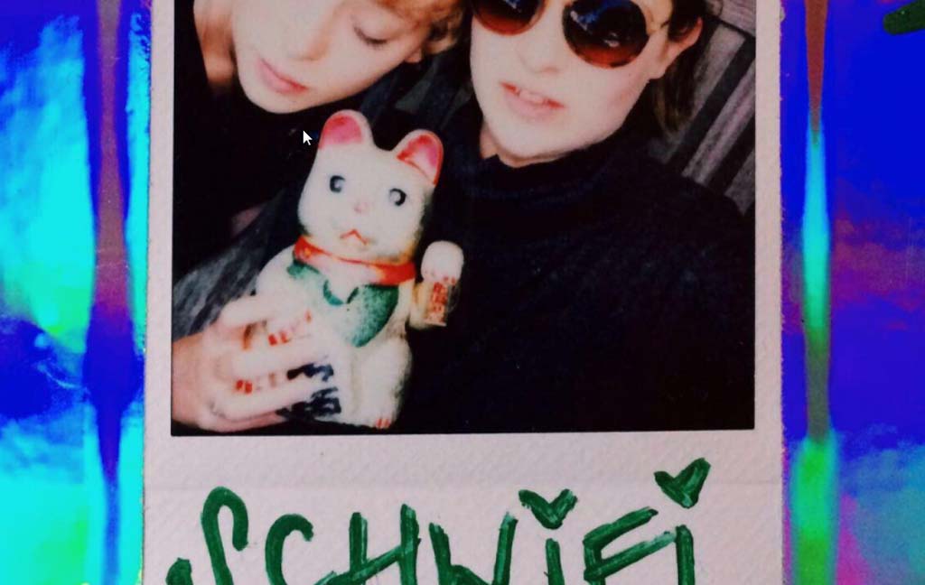 Polaroid von zwei Menschen und einer Winkekatze mit der Unterschrift "Schwifi".