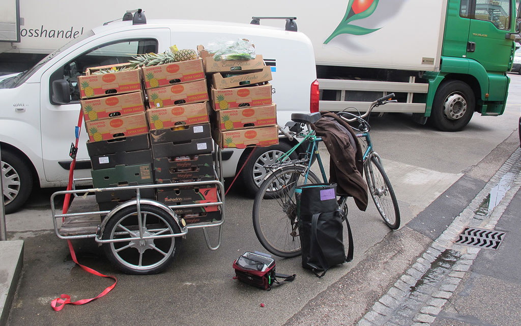 Fahrrad mit Anhänger, der mehr als voll mit Gemüseschachteln beladen ist.