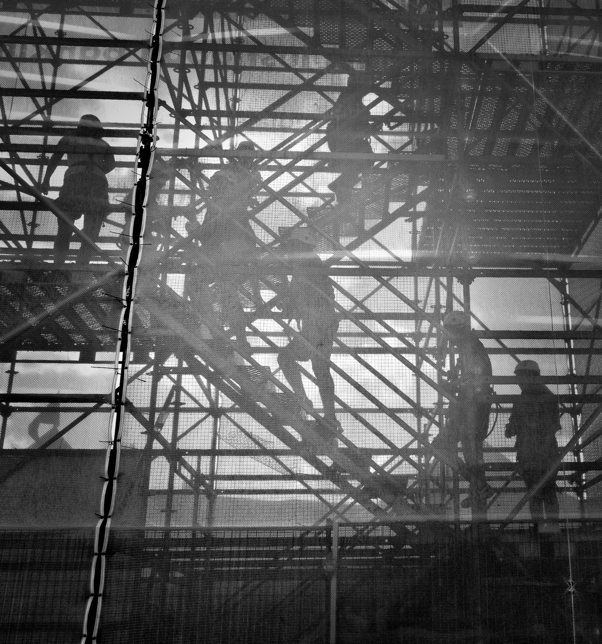 Schwarz-weiss Bild von Bauarbeitern auf einem Baugerüst an einer Betonwand.