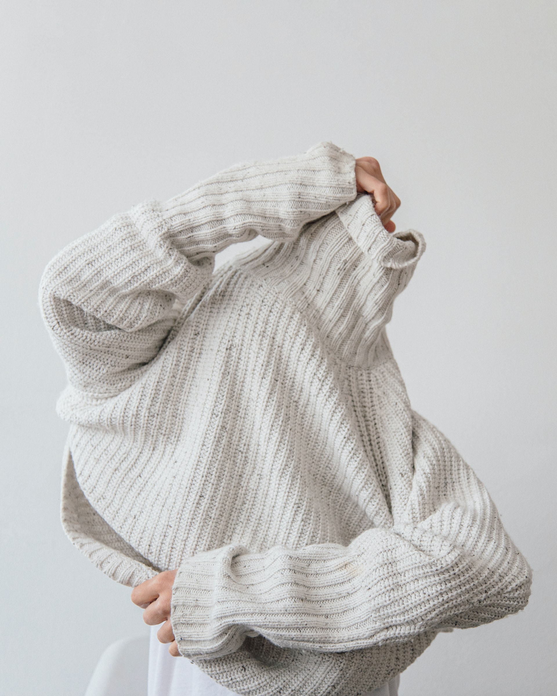 Mensch, der sich einen Strickpullover überzieht.