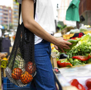 Person an einem Marktstand mit Gemüse in einer Netzttasche