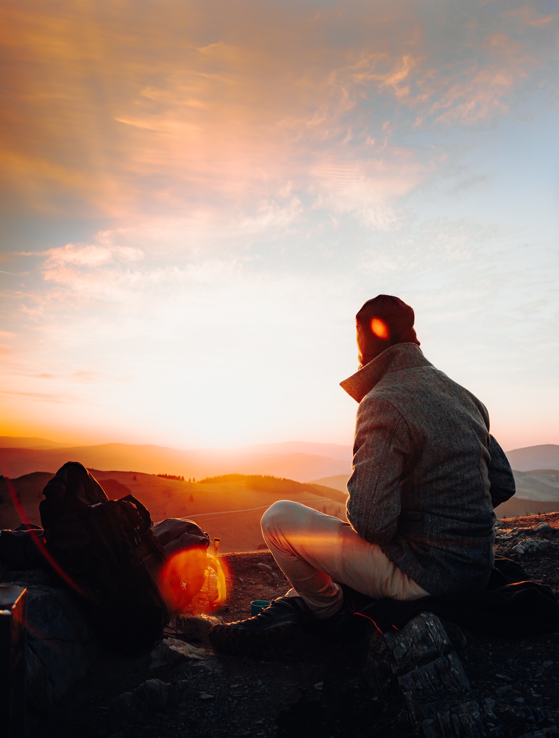 Ein Mensch sitzt draussen auf einer Anhöhe und schaut dem Sonnenuntergang vor natürlicher Kulisse zu.