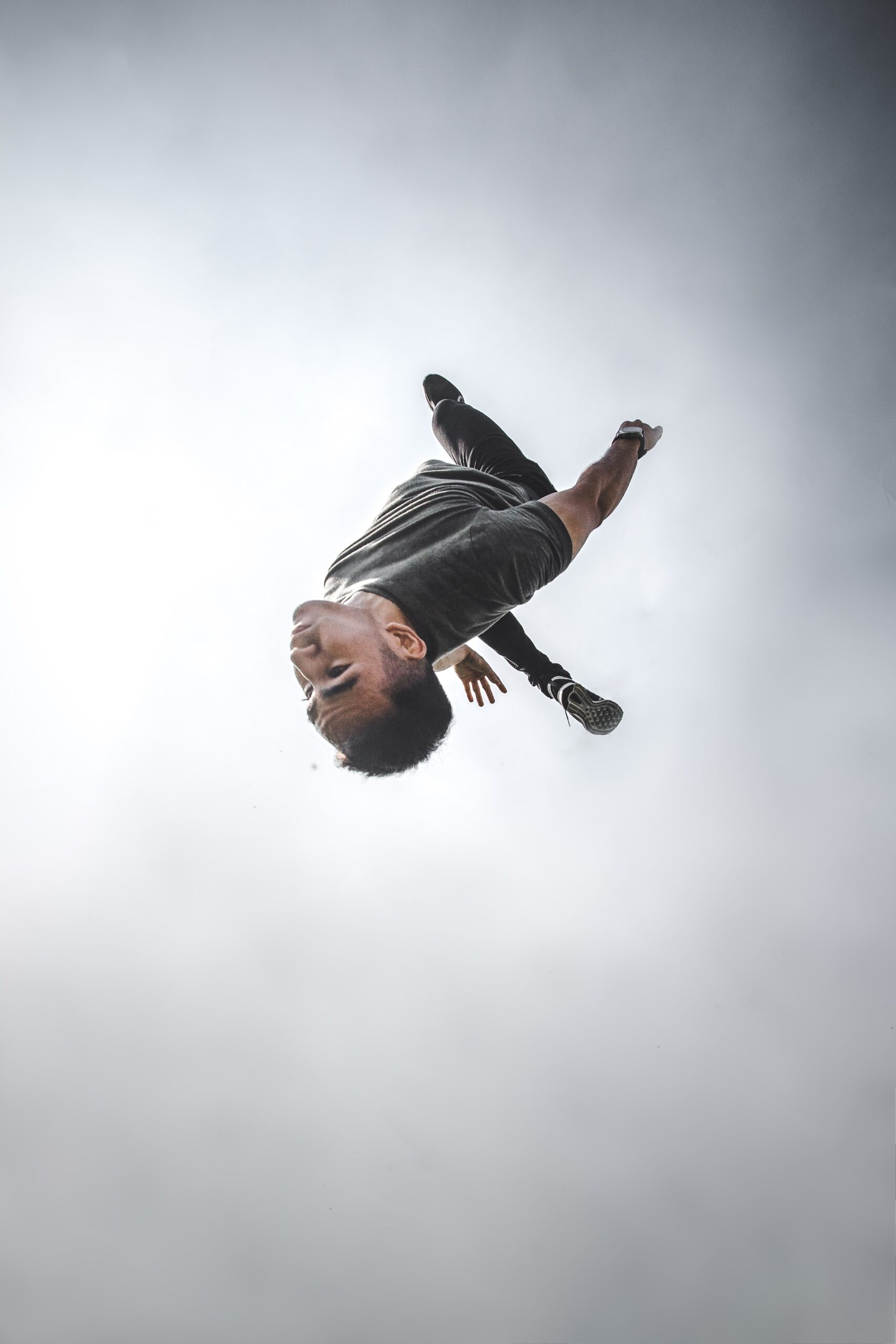 Ein springender Mann, fotografiert kopfüber, im Hintergrund Wolken