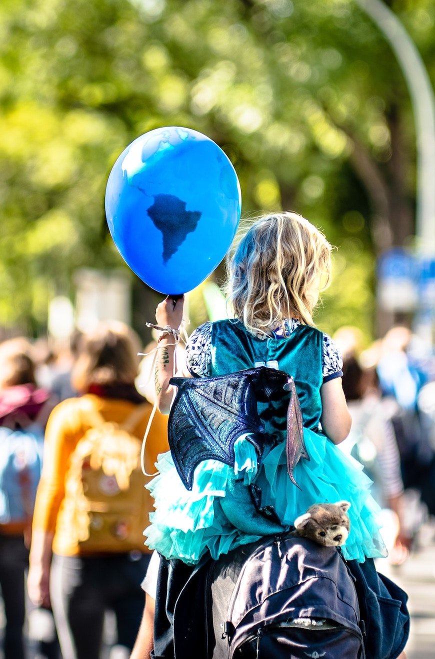 Kind mit blauem Ballon, der den Kontinent Afrika zeigt, auf den Schultern eines Erwachsenen in einem Protestmarsch.