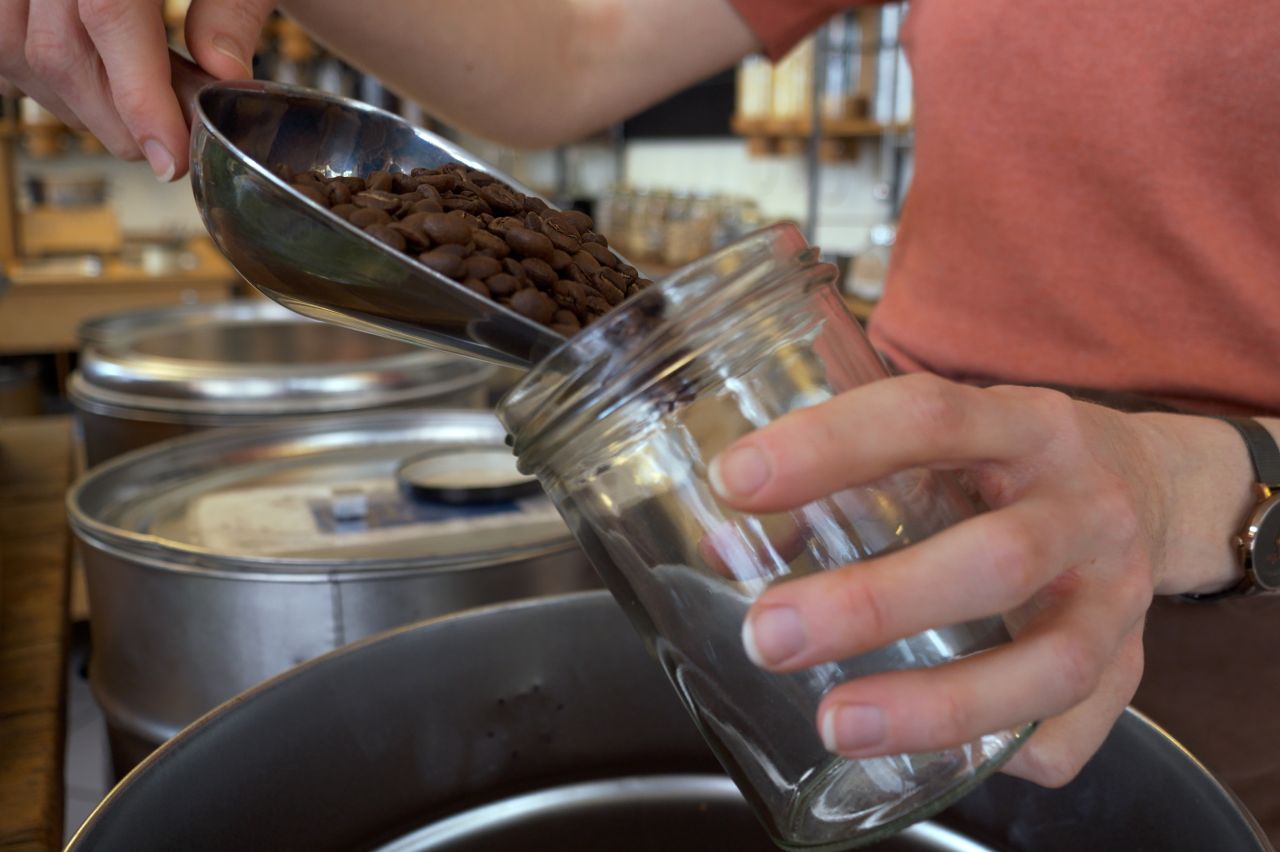 Person füllt Kaffeebohnen in ein Glas ab