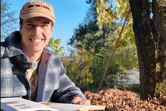 Luzius hält ein Buch in der Hand und schaut in die Kamera.
