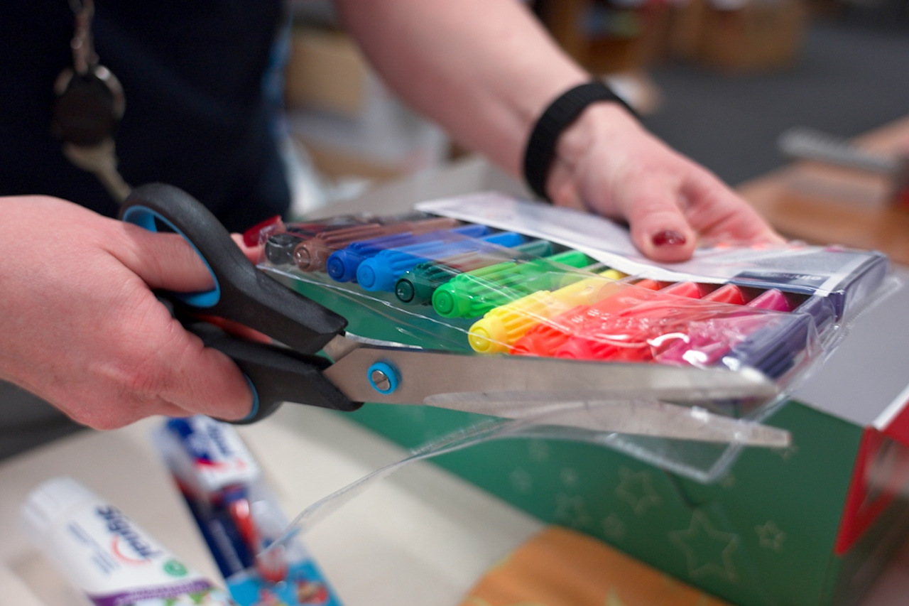 Eine Frau entfernt Plastikverpackungen von Stiften mit einer Schere.