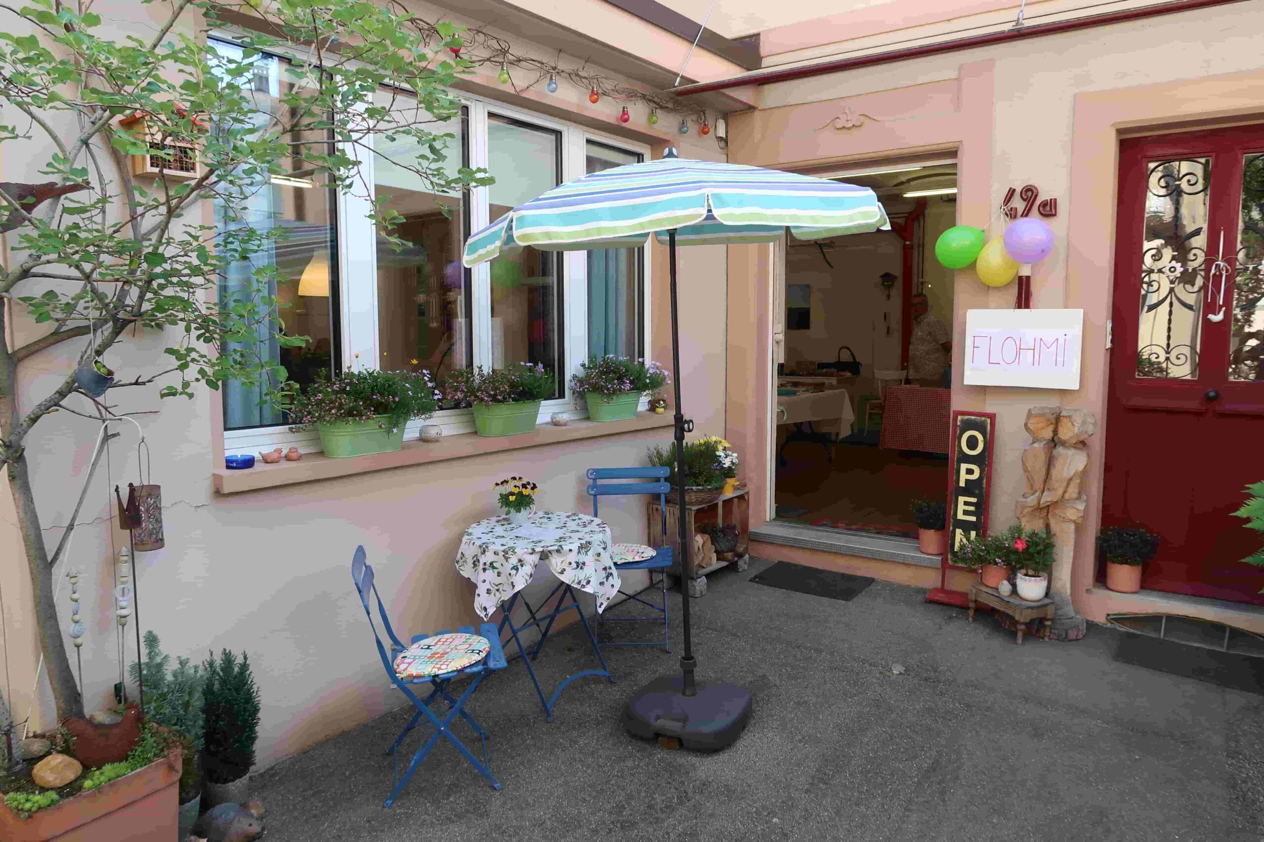 Eingangsbereich mit Sonnenschirm und Schild «Flohmi Open»